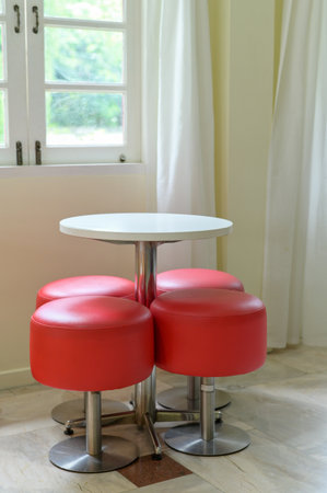 Vibrant red stool set with white round table offers modern furniture design for an indoor space. compact seating by bright window feels cheerful and invitingの写真素材