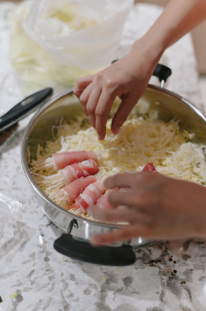 Hands preparing bacon wrapped enoki mushroom in stainless steel pan shredded cheese marble...