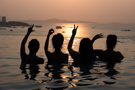 Silhouette of ladies show LOVE hands in a pool by the oceanの写真素材