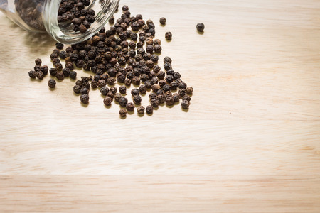 Black pepper spilled out on wooden background with copyspaceの写真素材