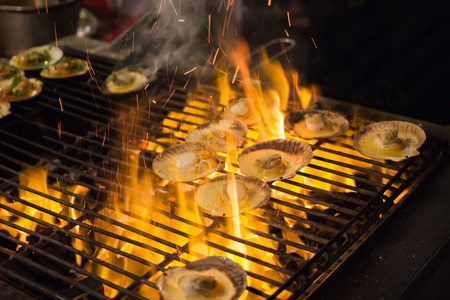 Grilled scallops topped with butter, garlic and parsley on a gridiron over fire at the seafood night marketの写真素材