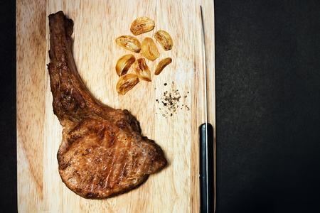 Delicious pork chop steak with spices and grilled garlic on wooden board; top viewの写真素材