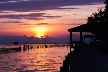 Silhouette of bridge along the sea coast and beautiful sunrise background with mussel farming and wooden house, livelihoods of fishermen in Thailandの写真素材