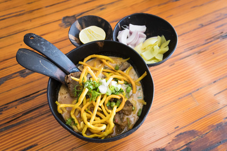 Khao Soi, Northern style curried noodle soup with beef in coconut shell bowl served with pickle lettuce, shallot, lemon and chili oil.の写真素材