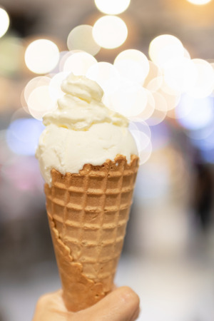 Crispy cone of a milky ice cream with a bokeh of festive party lights on background.の写真素材