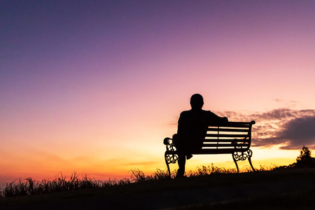 Silhouette of woman sitting alone on the bench against twilight sky over a mountain.の写真素材