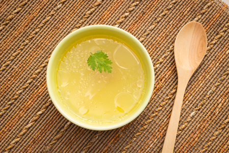 Bowl of chicken broth on rural table with wooden spoonの写真素材