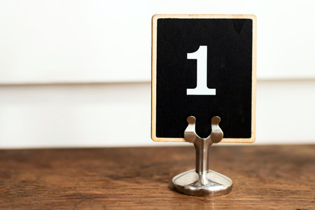 Number one on black label standing on wooden table with white wall on background.の写真素材