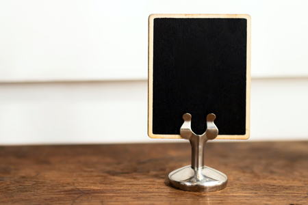 Black blank label standing on wooden table with white wall on background.の写真素材
