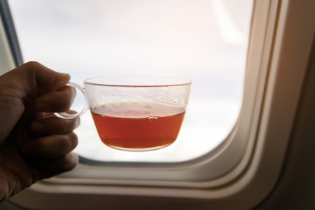 Hand hold cup of tea after meal and looking out of airplane, good time enjoying beautiful sky.の写真素材