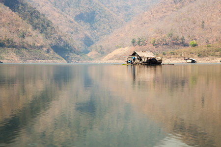 Fisherman wooden floating and drought mountain with reflection on river in Thailandの写真素材