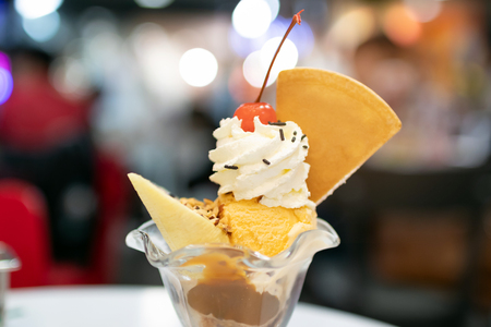 Vanilla and mocha ice cream sundae with chocolate flake, whipped cream and cherry on top on table with bokeh light background.の写真素材