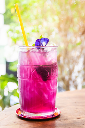 Butterfly pea with lemon juice on ice in transparent glass with summer garden background.の写真素材