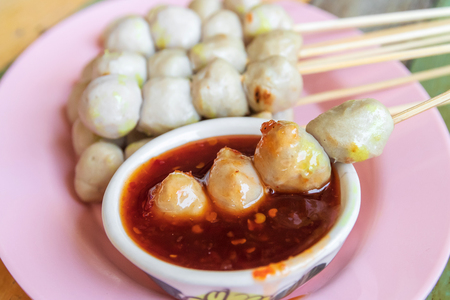 Grilled meatballs in bamboo skewers with sweet chili sauce served on plate on wooden retro table background.の写真素材