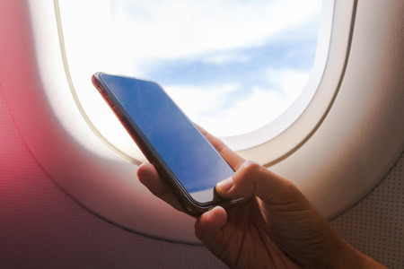Woman hand holding a smartphone on board; typing text message during flight, business travel,...
