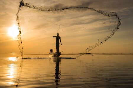 Silhouette of traditional fishermen throwing net fishing at sunrise time, livelihoods of fishermen at Pakpra, Phatthalung in Thailandの写真素材