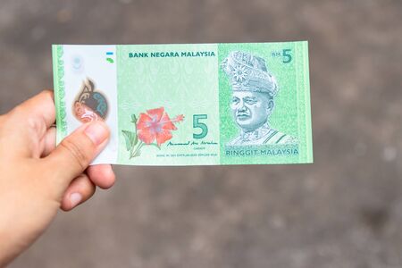 Five Ringgit Malaysia bank note on hand isolated on grey background.