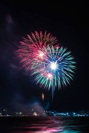 Fireworks over sea with city night on background. Festive colorful fireworks celebration in night sky.の写真素材