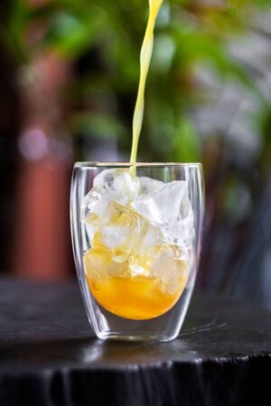 Pouring fresh orange juice on ice in glass on wooden table in a garden. Refresh your day.の写真素材