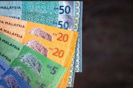 Various type of Malaysia Currency (MYR): Stack of Ringgit Malaysia bank note on dark brown a wooden table background. (There are one, five, twenty and fifty)の写真素材