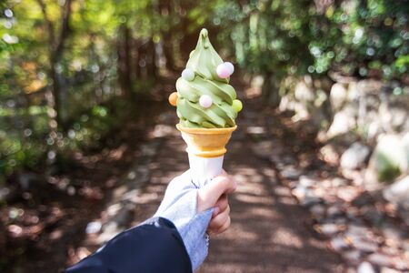 Woman hand holding green tea flavor soft serve cone with little ball candy on bokeh nature tree in a park.の写真素材