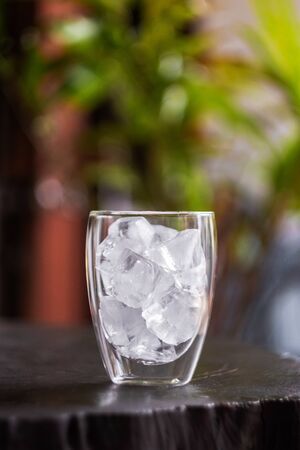 Glass with ice cubes on wooden table with green nature background.の写真素材