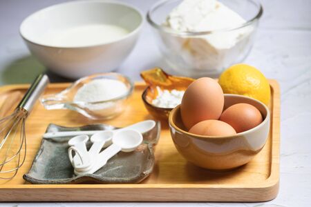Baking ingredients for cheesecake on wooden tray. Eggs, flour, sugar, lemon, cream, creamcheese and...