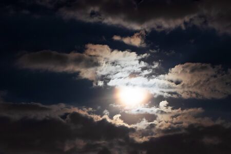 Full moon shining glowing light through the darkness of cloudy night sky; long exposure for...