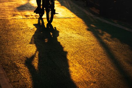 Silhouette of cyclist traveling on the road at sunset. Biking sports fitness athlete riding bike with sunlight and shadow. Active healthy sports lifestyle.の写真素材