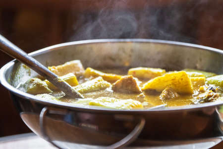 Yellow curry with fish and green taro (aaw dip) in hot pot on wooden table. Southern delicious food of Thailand.の写真素材