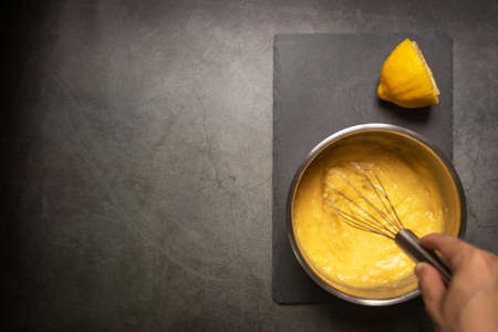 Chef whisking juicy lemon curd in a pot with copy space on black table background.の写真素材