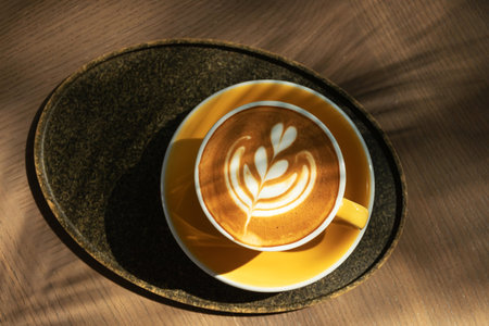 Cup of coffee with latte art on wooden table and morning sunlight with shadow through from window. Beautiful morning.の写真素材
