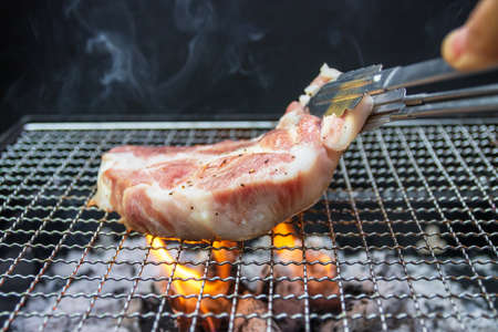 Charcoal grill pork steak with flames of fire and smoke on black background. Summer outdoor barbeque party or picnic concept.の写真素材