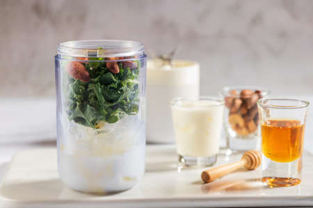 Healthy green kale smoothie in portable blender mixed greek yogurt, almond and honey on white table background. Kale is considered a superfood because it's a great source of vitamins and minerals.の写真素材