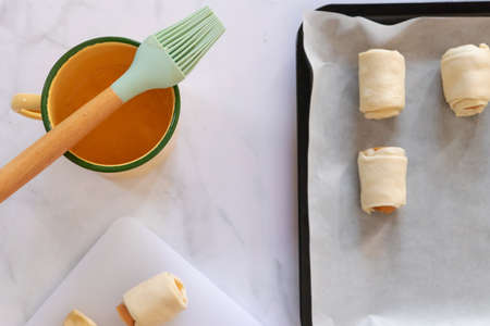 Mini sausage wrapped in puff pastry in oven tray prepare for bake. Beating the egg nicely and brush the top with it to get the shiny and smooth top.の写真素材