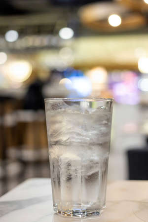 Glass of water with ice cubes on  table in blurred bokeh at restaurant.の写真素材