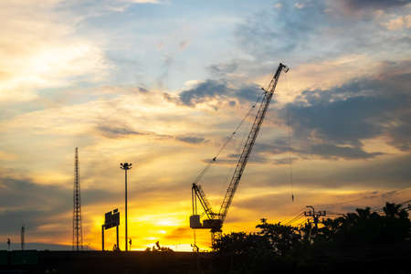 Silhouette of construction worker cranes with sunset sky background.