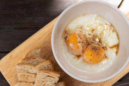Soft boiled egg with seasoning sauce and ground pepper with mini toast on wooden tray; top view.