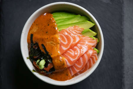 Salmon poke bowl with avocado and seaweed spicy sauce Japanese style. top view on black table background. Asian trendy food.の写真素材