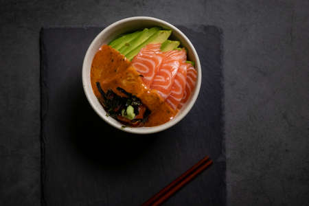 Salmon poke bowl with avocado and seaweed spicy sauce Japanese style. top view on black table...