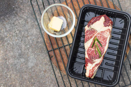 Strip loin steak with rosemary and butter prepared for barbeque grill. Top view and copy space.