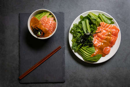 Salmon salad and salmon poke bowl with avocado and seaweed spicy sauce Japanese style on black table background. Asian trendy food.の写真素材