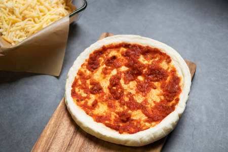 Pizza dough with ingredients on wooden board with black table background. Homemade delicious pizza....
