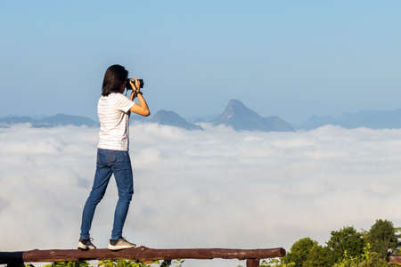 Young lady take photo with camera from top of a mountain with the sea of mist at Mon Kru Ba Sai, Mae Moei National Park, Tak in Thailand.の写真素材