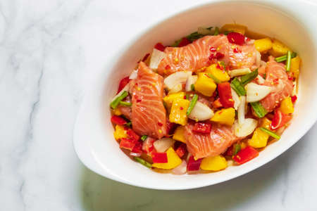 Spicy salmon mango salad in white oval bowl. Top view on white table with copy space.の写真素材