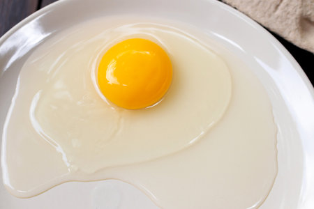 Organic free range egg and egg yolk on white dish; top view on wooden table background.の写真素材