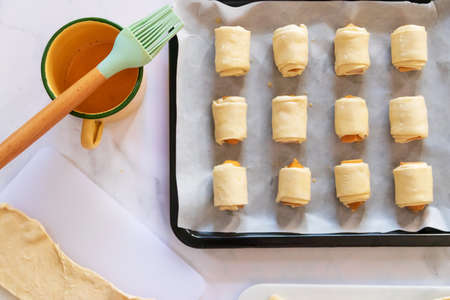 Mini sausage wrapped in puff pastry in oven tray prepare for bake. Beating the egg nicely and brush...