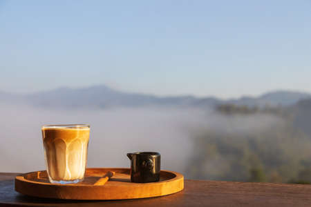 Sunrise coffee in nature. Dirty coffee on wooden table with mountain fog on shade of sunrise...