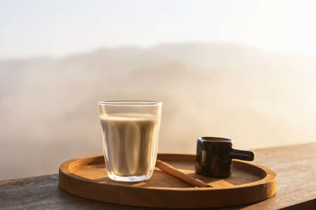 Sunrise coffee in nature. Milk with coffee shot on wooden table with mountain fog on shade of...