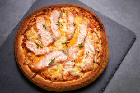 Delicious gourmet pizza with salmon on board with black table background. Homemade delicious pizza. Top view and copy space.の写真素材